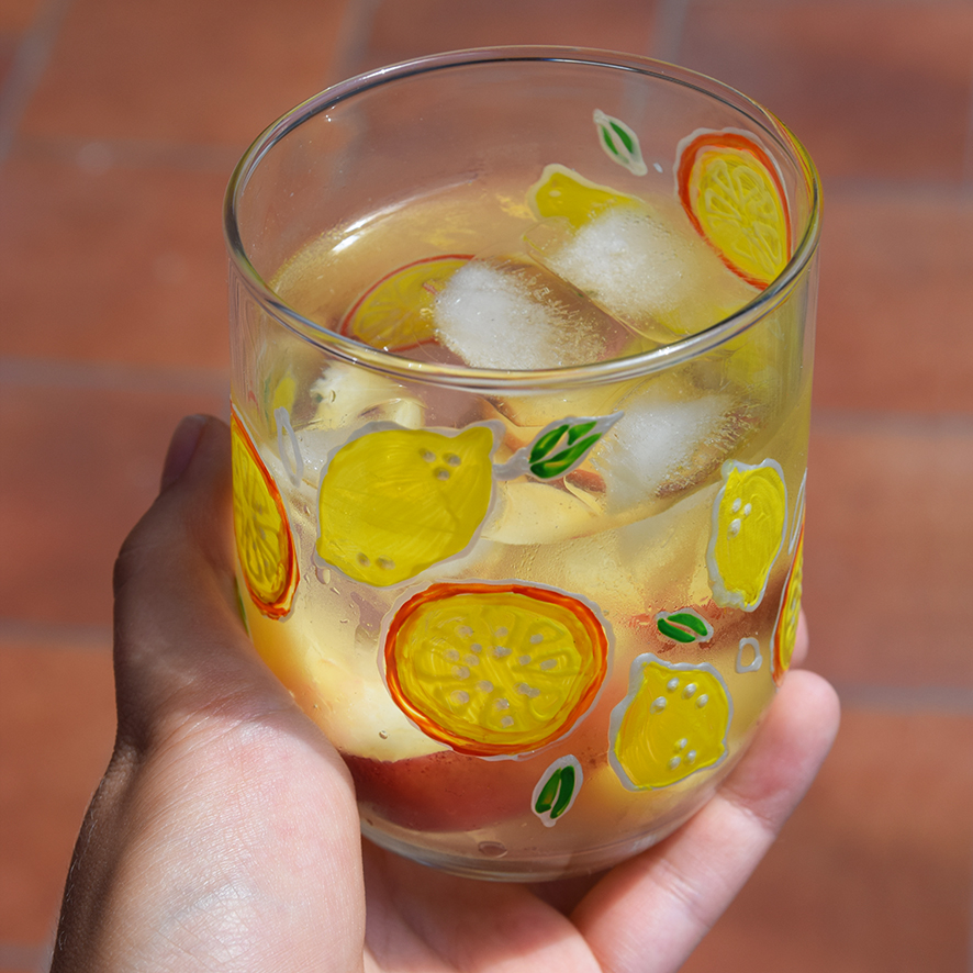 Žena drž&iacute; v ruke maľovan&yacute; ovocn&yacute; poh&aacute;rik na limon&aacute;du a vychutn&aacute;va si drink.